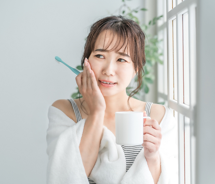 Woman in bathrobe holding coffee cup and rubbing jaw in pain