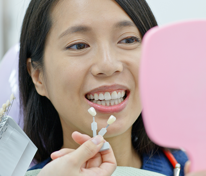 Woman checking smile in handheld mirror after cosmetic dentistry in Fort Lee